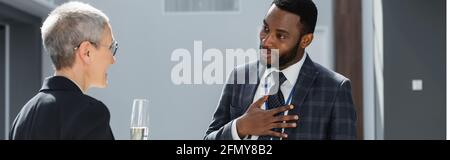 homme d'affaires afro-américain tenant la main sur la poitrine tout en parlant à son collègue, banner Banque D'Images