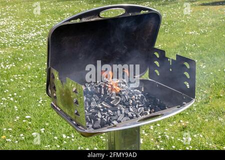 Un barbecue à charbon de bois chaud et vide avec feu ouvert. Préparation d'un délicieux barbecue extérieur sur un pré vert avec des pâquerettes le jour de printemps ensoleillé. BARBECUE Banque D'Images