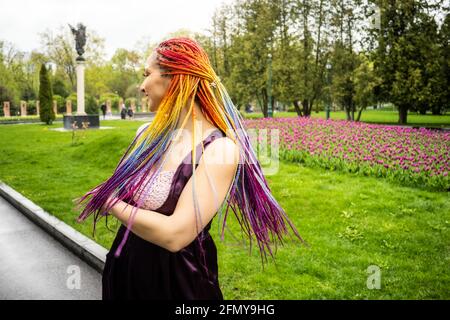 Une belle fille avec un maquillage multicolore à paillettes et des tresses africaines brillantes dans une robe en satin violet. Elle sourit doucement et se réjouit à l'arrivée o Banque D'Images