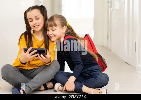 Deux camarades d'école modernes jouant dans un smartphone pendant une pause entre les leçons Banque D'Images