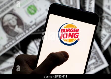 Sur cette photo, le logo Burger King de la chaîne américaine de restaurants de restauration rapide de hamburger est affiché sur un smartphone avec une devise américaine (dollar américain) en arrière-plan. Banque D'Images