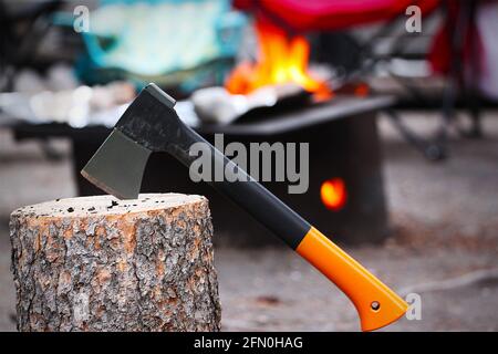 Hache coincé sur la souche d'arbre avec le bois de chauffage brûlant dans le foyer de camping en arrière-plan. Camping en plein air dans le parc national Banff. Mise au point sélective sur la perte Banque D'Images