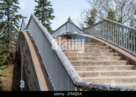 Un pont en porte-à-faux en béton d'époque s'étendant sur un chemin dans un parc. Le pont en béton comporte des marches de part et d'autre avec une main courante en métal gris Banque D'Images