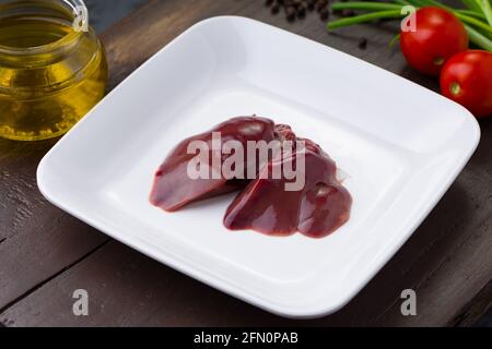 Foie de poulet cru joliment disposé dans une plaque en céramique blanche avec de la petite tomate, de l'oignon de printemps et de l'huile de cuisson sur fond Banque D'Images
