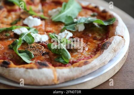 Pizza italienne à salade de saucisses et de roquette sur fond de bois Banque D'Images