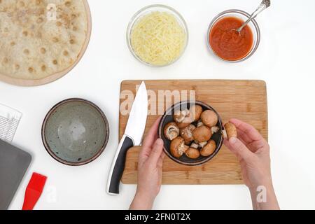 Les champignons Criminaux dans un bol se ferment sur une table de cuisine. Pizza avec mozzarella et recette de champignons, plat, mains de femme Banque D'Images