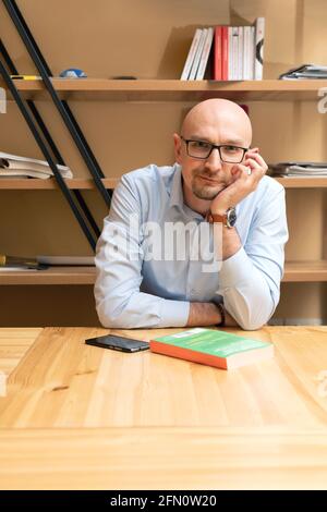 Souriant homme chauve sympathique portant des lunettes avec livre regardant appareil photo Banque D'Images