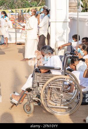 Anuradhapura, Sri Lanka - 03 31 2021: Vieille dévot en fauteuil roulant adorant les deux mains sur son front au temple Jaya Sri Maha Bodhi. Banque D'Images