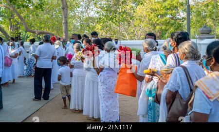 Anuradhapura, Sri Lanka - 03 31 2021: De nombreux pèlerins en vêtements blancs en ligne pour offrir des fleurs à Jaya Sri Maha Bhodi. Banque D'Images