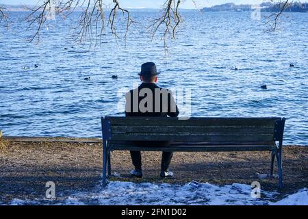 Un homme vêtu de noir est assis sur un banc sur la rive du lac Starnberg à Tutzing, un après-midi frais d'hiver. Banque D'Images