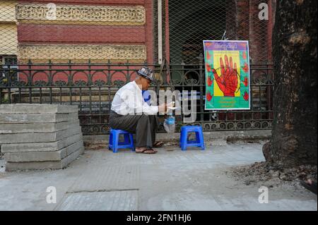 02.04.2014, Yangon, Myanmar, Asie - UN palmiste se trouve sur un tabouret en plastique à côté de la route dans l'ancienne capitale et attend les clients. Banque D'Images