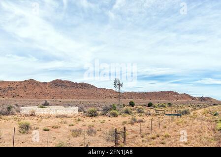 Un moulin à vent et un barrage à côté de la route N1 entre Richmond et Three Sisters dans le nord du cap Karoo. Une croix et un mot sont visibles contre une colline Banque D'Images