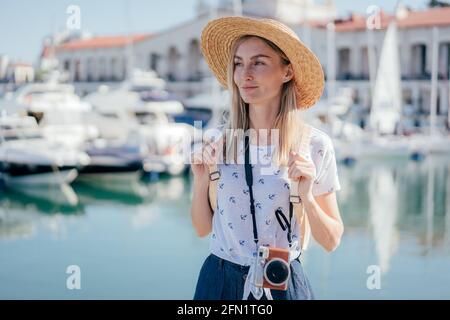 Jeune femme attrayante voyageur dans un chapeau de paille avec un appareil photo marche dans le port maritime. Banque D'Images