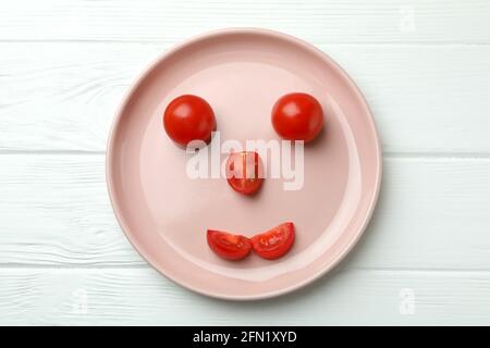 Assiette avec Happy face faite de tomates sur bois blanc arrière-plan Banque D'Images