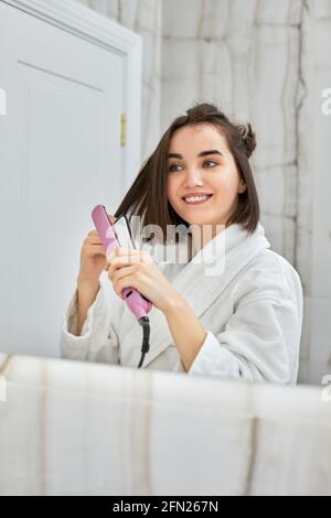 femme utilisant un lisseur dans la salle de bains. Banque D'Images