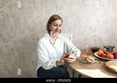 Une femme adulte s'assoit dans la cuisine à la table et regarde le téléphone. Banque D'Images