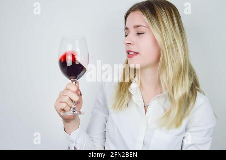 Portrait d'une belle jeune femme blonde tournoyant le rouge vin dans le verre pour aérer le vin et libérer son bouquet lors d'une dégustation de vin Banque D'Images