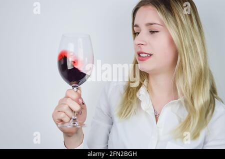 Portrait d'une belle jeune femme blonde tournoyant le rouge vin dans le verre pour aérer le vin et libérer son bouquet lors d'une dégustation de vin Banque D'Images