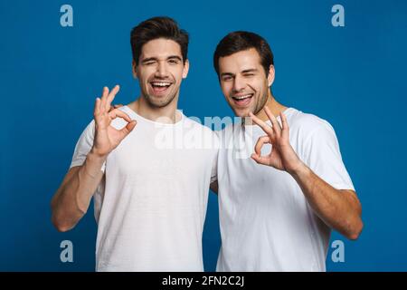 Heureux non rasé deux gars wencen tout en montrant des signes ok isolés sur fond bleu Banque D'Images