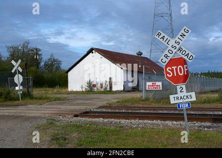 Traversée de chemins de fer ruraux en Alaska (États-Unis) avec panneau d'arrêt et panneau typiques Railroad Crossing, ainsi qu'un ancien hangar en étain et un mât radio à l'arrière Banque D'Images