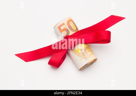 Un rouleau de billets en euros entouré d'un ruban rouge et d'un joli noeud. Ruban coloré entourant les billets en euros. Donner de l'argent comme cadeau. Pour faire un don à un Banque D'Images