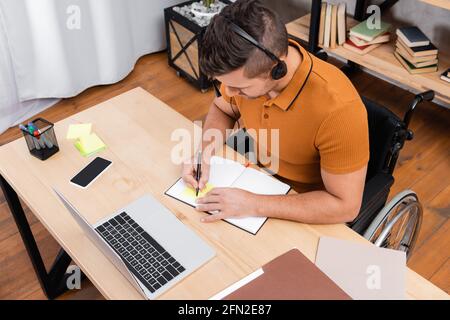 vue en hauteur de l'homme handicapé qui écrit sur son micro-casque/oreillette sur son ordinateur portable Banque D'Images