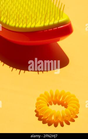 Peigne à cheveux en plastique jaune orange et attache en plastique jaune sur table jaune ensoleillée. Banque D'Images
