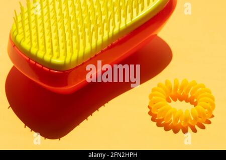 Peigne en plastique et serre-cheveux sur une table jaune ensoleillée. Banque D'Images