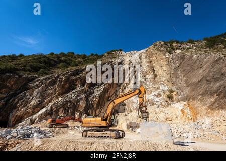 Pelles hydrauliques à chenilles orange avec marteau perforateur dans une carrière de marbre blanc. Alpes Apuanes (Alpi Apuane), province de Massa et Carrara, Toscane, Italie, Europe. Banque D'Images