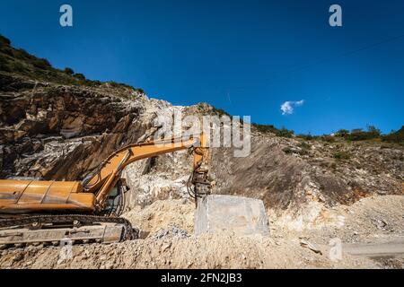 Pelle hydraulique à chenilles orange avec marteau piqueur dans une carrière de marbre blanc. Alpes Apuanes (Alpi Apuane), province de Massa et Carrara, Toscane, Italie, Europe. Banque D'Images