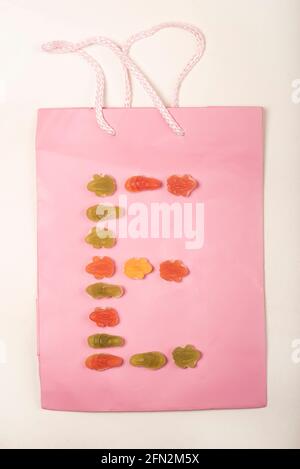 Lettres de l'alphabet colorées faites d'un arrangement de bonbons (bonbons) sur un sac cadeau rose, mis sur un fond blanc. Banque D'Images