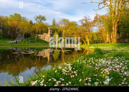 Photo prise dans le parc Nicolae Romanescu de Craiova, Roumanie au coucher du soleil. La photo se compose d'un étang, d'un pré avec des fleurs et d'un pont suspendu Banque D'Images