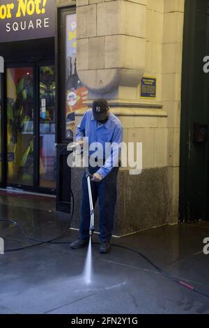 Un ouvrier de l'entretien des bâtiments nettoie le trottoir avec un pulvérisateur d'eau de grande puissance dans Midtown Manhattan, New York. Banque D'Images