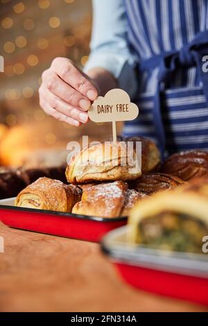 Gros plan de l'adjoint aux ventes de la boulangerie mettre les produits laitiers en vente libre Étiquetez dans une pile de petits pains à la cannelle fraîchement cuits Banque D'Images