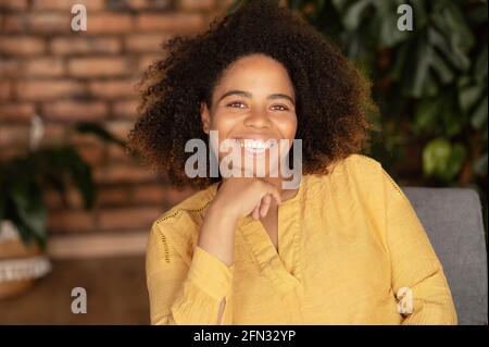 Photo d'une jeune femme afro-américaine hilarante, charmante femme noire regarde l'appareil photo avec un grand sourire joyeux, un portrait d'une jeune fille ethnique attrayante à la maison, un concept de santé et de bien-être Banque D'Images