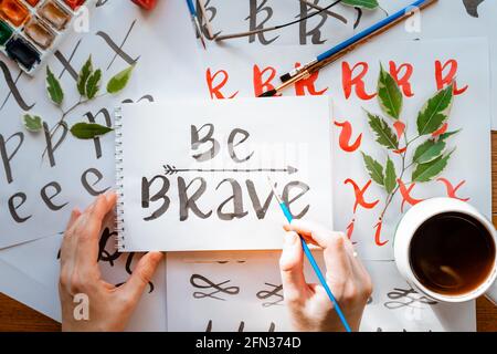 Vue de dessus sur hommes mains calligraphie feuilles, niches, papier, encre rouge stylos.artisanat, passe-temps. Lettering workshop.Flat lay lettres de motivation mots quo Banque D'Images