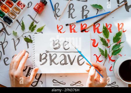 Vue de dessus sur hommes mains calligraphie feuilles, niches, papier, encre rouge stylos.artisanat, passe-temps. Lettering workshop.Flat lay lettres de motivation mots quo Banque D'Images