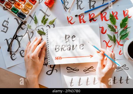 Vue de dessus sur hommes mains calligraphie feuilles, niches, papier, encre rouge stylos.artisanat, passe-temps. Lettering workshop.Flat lay lettres de motivation mots quo Banque D'Images