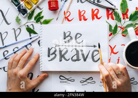 Vue de dessus sur hommes mains calligraphie feuilles, niches, papier, encre rouge stylos.artisanat, passe-temps. Lettering workshop.Flat lay lettres de motivation mots quo Banque D'Images