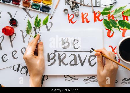 Vue de dessus sur hommes mains calligraphie feuilles, niches, papier, encre rouge stylos.artisanat, passe-temps. Lettering workshop.Flat lay lettres de motivation mots quo Banque D'Images