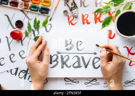 Vue de dessus sur hommes mains calligraphie feuilles, niches, papier, encre rouge stylos.artisanat, passe-temps. Lettering workshop.Flat lay lettres de motivation mots quo Banque D'Images