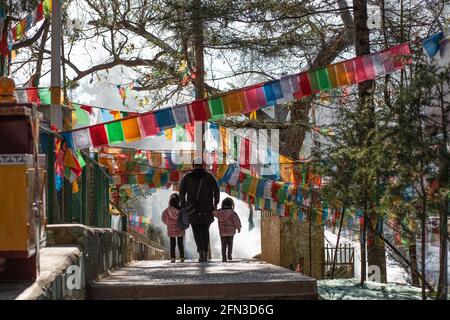 Femme vue de derrière marchant avec ses deux enfants au milieu des drapeaux de prière.Shangri la, Yunan. République populaire de Chine 2019 Banque D'Images