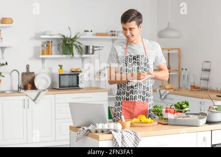 Jeune homme avec ordinateur portable dans la cuisine Banque D'Images