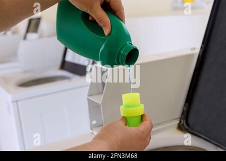 Une femme verse de la poudre liquide, verse du conditionneur, emollient dans de la machine à laver. Banque D'Images