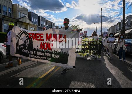 Philadelphie, États-Unis. 13 mai 2021. Deux personnes détiennent une bannière demandant la libération de Mumia Abu-Jamal, journaliste et activiste reconnu coupable du meurtre d'un policier de Philadelphie en 1981 et qui est toujours incarcéré. Ils se sont joints à d'autres résidents de l'ouest de Philadelphie qui ont défilé sur Pine Street pour marquer le 36e anniversaire de la mort de la famille africaine, membres de l'organisation MOVE, lorsque la police de Philadelphie a déposé une bombe dans leur maison. Crédit : Kylie Cooper/Alay Live News Banque D'Images