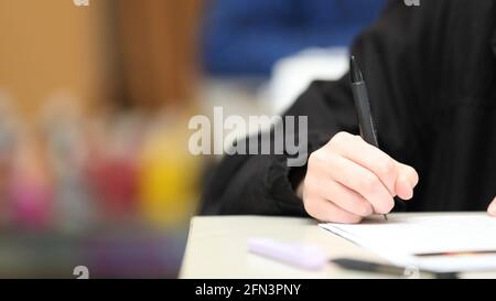 Un gros plan isolé élèves main tenant un stylo écrivant pendant la classe, l'examen ou le temps de leçon à l'école. Couleurs vives et deuxième élève flou dans le b Banque D'Images