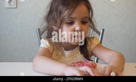 La petite fille mignonne heureuse mange du beignet. L'enfant s'amuse avec du beignet. Nourriture savoureuse pour les enfants. Un moment amusant à la maison avec de la nourriture douce. Enfant brillant. Faire un don Banque D'Images