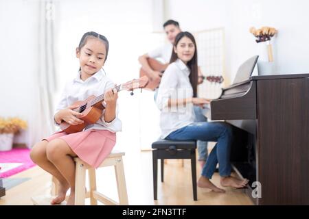 Famille asiatique, fille jouant ukulele, père jouant de la guitare, mère jouant du piano dans le groupe familial à la maison, concept pour la relation familiale Banque D'Images