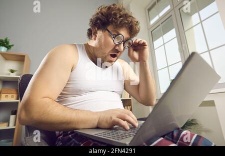 Surprise drôle choqué gros homme en pyjama lit des nouvelles étonnantes sur ordinateur portable Banque D'Images