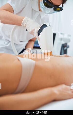 Dermatologue professionnel effectuant l'épilation au laser sur les jambes du patient Banque D'Images